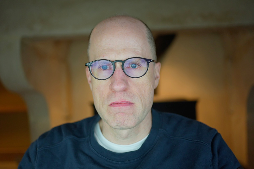 Outdoors half-figure portrait of Nick Bostrom in autumn-coloured clothes in front of an old building in the daytime