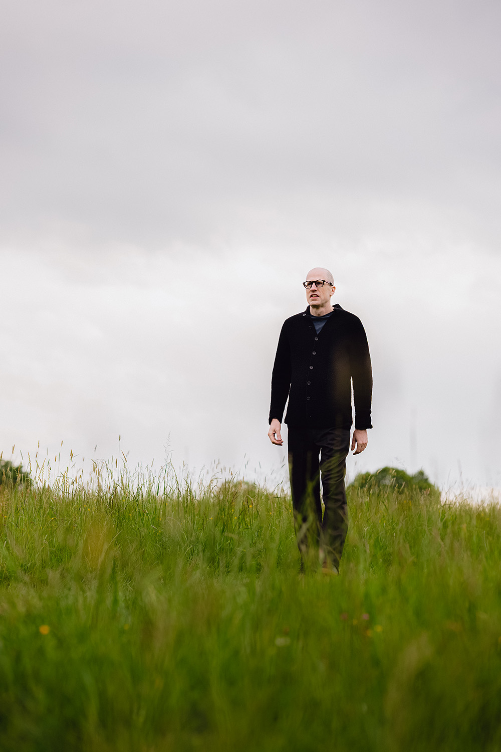 Outdoors portrait of Nick Bostrom walking across a grassy field